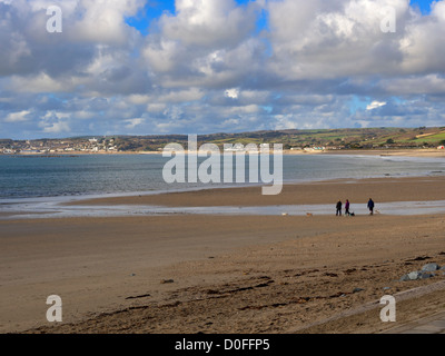 Mounts Bay Strand und Penzance von Marazion, Cornwall. Drei Personen Spaziergang mit seinem Hund am Strand im Herbst. Stockfoto