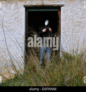 Mann mit weißer Maske von gebrochenen Tür des verlassenen Haus und verwilderten Pflanzen. Stockfoto