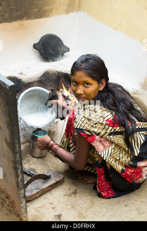 Junge Süd indische Frau kochende Milch auf einem offenen Feuer in ihrem ländlichen Dorf nach Hause. Andhra Pradesh, Indien Stockfoto