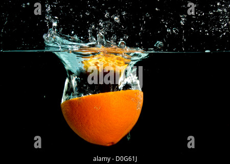 Spritzer orange Frucht ins Wasser auf schwarz Stockfoto