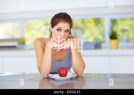 Eine attraktive junge Frau suchen enttäuscht mit dem roten Apfel auf ihrem Teller Stockfoto