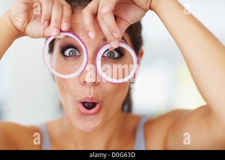 Eine attraktive junge Frau hält einen Zwiebel Ring vor jedem Auge Stockfoto