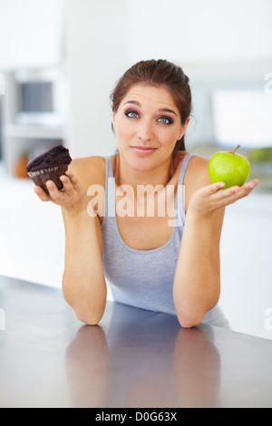 Eine attraktive junge Frau hält einen Cupcake und ein Apfel Stockfoto