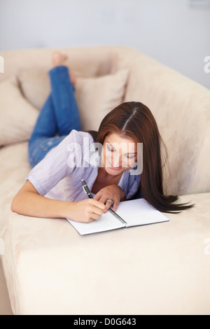 Eine attraktive junge Frau in einem Buch zu schreiben, wie sie auf einer Couch liegt Stockfoto