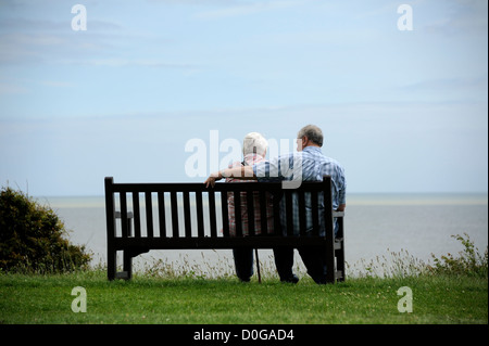 Ein älteres Ehepaar blicken auf das Meer von einer Parkbank im Vereinigten Königreich. Stockfoto