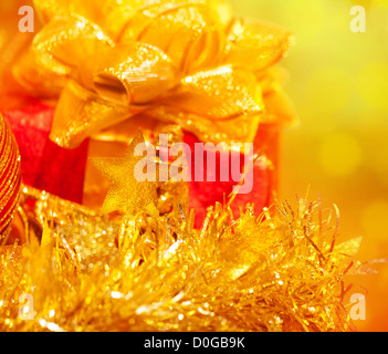 Foto von Weihnachtsgeschenk, rote Geschenkbox mit großen goldenen Bogen auf gelben Unschärfe Hintergrund, Chritmastime Urlaub, Sterne Dekoration Stockfoto