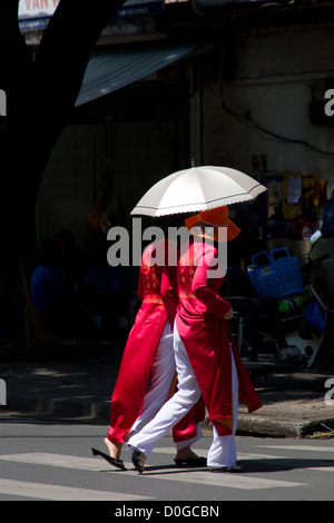 Zwei Frauen in traditioneller Tracht überqueren einer Straße in Ho-Chi-Minh-Stadt, Vietnam. Stockfoto