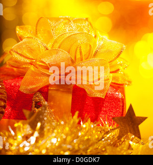 Foto von Weihnachtsgeschenk, rote Geschenkbox mit großen goldenen Bogen auf gelben Unschärfe Hintergrund, Chritmastime Urlaub, Sterne Dekoration Stockfoto