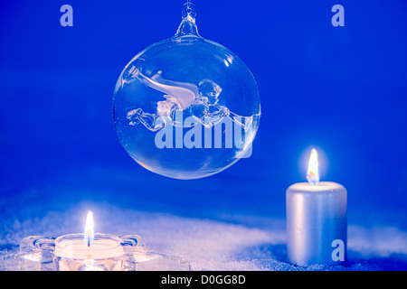 Magische Nacht mit Weihnachtsschmuck im Kerzenlicht. Engel-Christbaumkugel und Kerzen auf Schnee. Stockfoto