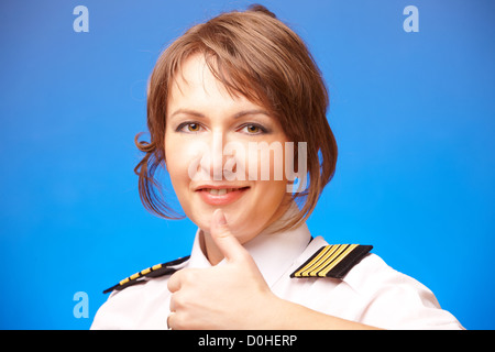 Schöne Airline-Piloten in Uniform mit Epauletes Daumen Geste der Zustimmung, stehend auf blauem Hintergrund angezeigt. Stockfoto