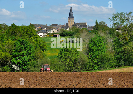 Ein Traktor pflügt ein Feld in der Nähe eines Dorfes in Frankreich (Mayenne Oisseau, Norden, Pays de la Loire, Frankreich). Stockfoto