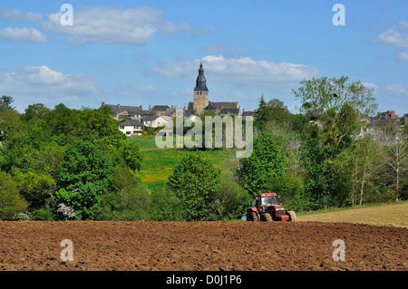 Ein Traktor Pflügen eines Feldes vor einem französischen Dorf (Norden Mayenne, Pays de la Loire, Frankreich, Europa). Stockfoto