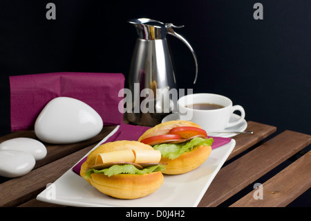 Zwei Sandwich auf weißen Porzellanteller, Tasse Tee und Thermoskanne auf Tisch Stockfoto