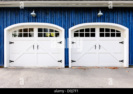 Zwei weiße Garagentore und Fenster im blauen Haus Stockfoto