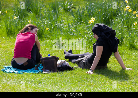 Zwei Frauen Faulenzen auf der Wiese inmitten Frühjahr Narzissen in Christus Kirche College Meadows in Oxford. Stockfoto