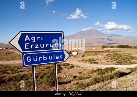 Ein türkisches Straßenschild in der Nähe des Berges Ararat oder Agri Dagi, ein schneebedecktes, schlafendes Vulkanmassiv, ragt über einem winzigen Dorf in Ostanatolien, Türkei, auf. Stockfoto