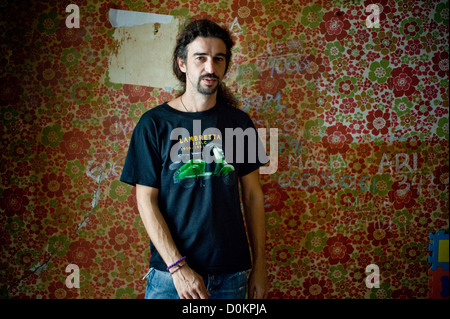 Kaukasischen Mann mit langen, dunklen Haaren posiert vor eine alten und bunten Wand. Stockfoto