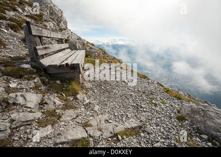 Bei Sitzbank am Rande eines felsigen Berges mit Blick auf Innsbruck, die unter den Wolken unten im Tal ist. Stockfoto