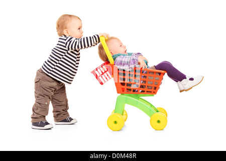 Kleinkind Jungen Drängen seiner Zwillingsschwester in ein Spielzeug-Cart isoliert auf weißem Hintergrund Stockfoto