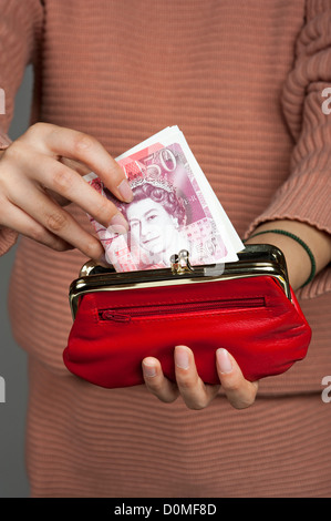 Zarte Frauenhand mit fünfzig Pfund Banknoten und eine rote Handtasche britische Sterling Stockfoto