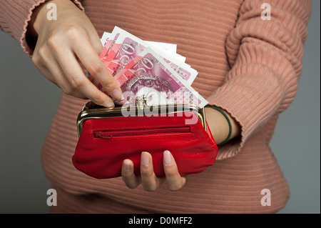 Zarte Frauenhand mit fünfzig Pfund Banknoten und eine rote Handtasche britische Sterling Stockfoto