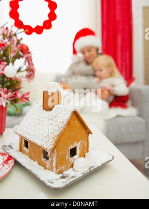 Closeup auf Weihnachten Lebkuchenhaus und Mutter und Baby mit Tablet PC im Hintergrund Stockfoto