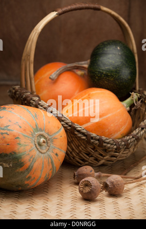 Reife orange Kürbisse in ländlichen geflochtenen Korb und Mohnköpfen auf Holztisch Stockfoto