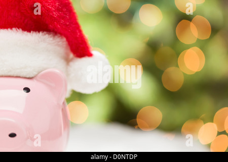 Rosa Sparschwein mit roten und weißen Weihnachtsmütze auf Schneeflocken mit abstrakten Hintergrund - Raum für Ihren eigenen Text. Stockfoto