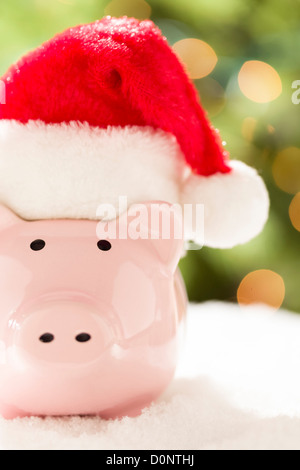 Rosa Sparschwein mit roten und weißen Weihnachtsmütze auf Schneeflocken mit abstrakten grünen und goldenen Hintergrund. Stockfoto