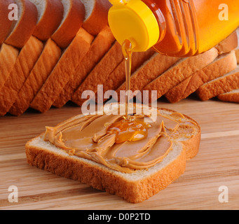 Nahaufnahme, ein Erdnussbutter und Honig Sandwich zu machen. Scheibe Brot mit PB bereits ausgebreitet und Honig auf gegossen wird. Stockfoto