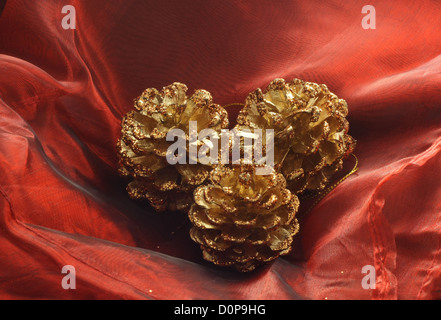 drei vergoldeten Pinienzapfen als Weihnachtsdekoration platziert auf Seide rot Stockfoto