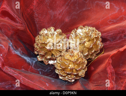 drei vergoldeten Pinienzapfen als Weihnachtsdekoration platziert auf Seide Stockfoto