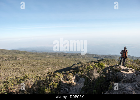 KILIMANDSCHARO, Tansania – Ein Kilimandscharo-Reiseleiter steht auf einem Felsvorsprung mit Blick auf ein Tal auf der Mweka-Route. Stockfoto