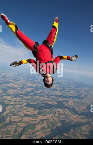 Fallschirmspringer Mädchen fliegt in einer kopfüber-Position über eine schöne Felder Fläche. Sie ist Spaß und fallen mit einer Geschwindigkeit von 125 km/h. Stockfoto