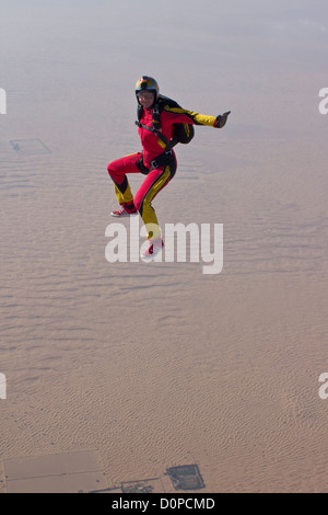 Fallschirmspringer-Mädchen in einer Sit-up-Position fällt frei durch den blauen Himmel über ein trockenes Wüstengebiet mit einem Lächeln auf ihr Gesicht. Stockfoto