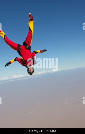 Fallschirmspringer-Mädchen in einem Kopf unten Position fällt frei durch den blauen Himmel über ein trockenes Wüstengebiet mit einem Lächeln auf ihr Gesicht. Stockfoto