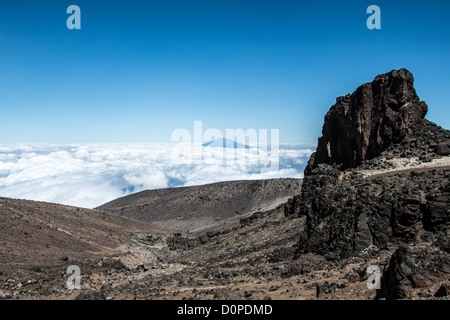 MOUNT KILIMANJARO, Tansania – der Gipfel des Mount Meru ragt durch die Wolkendecke, vom Arrow-Gletscher aus gesehen, entlang der Lemosho-Route des Mount Kilimanjaro. Der Mount Meru, Tansanias zweithöchster Gipfel mit 4.566 Metern, liegt etwa 70 Kilometer südwestlich des Mount Kilimanjaro im Arusha-Nationalpark. Die Lemosho-Route gilt weithin als einer der malerischsten Zugänge zum Gipfel des Kilimandscharo, bekannt für ihre vielfältigen Landschaften und ihr allmähliches Akklimatisierungsprofil. Der Arrow Glacier liegt auf etwa 4.900 Metern Höhe an den westlichen Hängen des Kilimandscharo und bietet weitläufige Aussichten Stockfoto