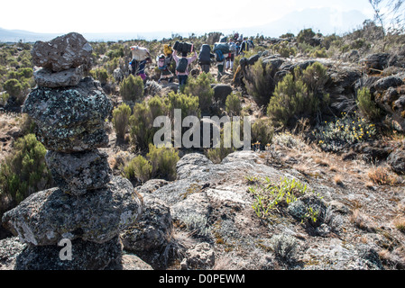 DER KILIMANDSCHARO, Tansania – Ein Steinhaufen neben dem Pfad der Lemosho-Route auf dem Kilimandscharo, während eine Gruppe von Trägern vorbeigeht. Stockfoto