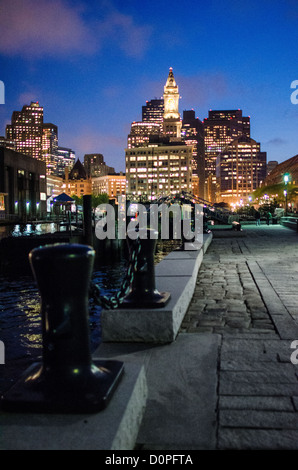 Ansicht der Innenstadt von Boston in der Nacht von Long Wharf. In der Mitte des Rahmens ist der hohe Marriot Custom House Hotel Clock Tower. Auf der linken Seite sind einige der die feste Poller entlang der Anlegestelle für Schiffe bis zu binden. Stockfoto