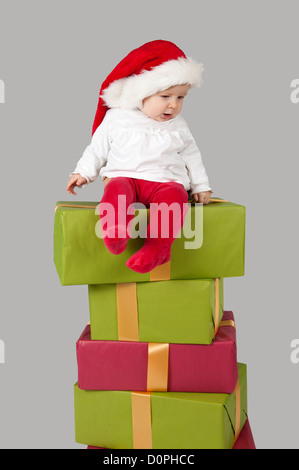 Baby sitzt auf einem Stapel von Weihnachten präsentiert, isoliert auf grau Stockfoto