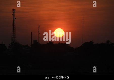 VIENTIANE, Laos – die untergehende Sonne bildet Kommunikationstürme und Bäume am anderen Ufer des Mekong. Da die Wasserstraße hier die internationale Grenze bildet, liegt die sichtbare Landmasse vollständig in der thailändischen Provinz Nong Khai. Vientiane ist nach wie vor eine der wenigen Hauptstädte, die direkt an einer Grenze liegt, eine Geographie, die durch 1893 französische Kolonialverträge festgelegt wurde, die die lao sprechende Bevölkerung der Region formell trennten. Stockfoto