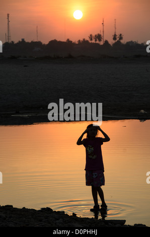 VIENTIANE, Laos - eine junge LAOTISCHE Mädchen spielt in den seichten, noch Wasser des Mekong Flusses und ist gegen die untergehende Sonne in der Entfernung. Vientiane, Laos. Stockfoto