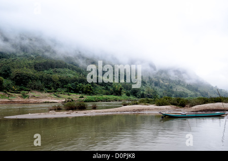 Nam-ou-Fluss Karst Landschaft Nong Khiaw Laos // NONG KHIAW, Laos — Nebel umhüllen die steilen Kalksteinkarste entlang der Ufer des Nam-ou-Flusses in Nong Khiaw im Norden Laos. Sandbänke in der Mitte des Flusses bilden kleine Sandinseln und geschützte Anlegeplätze für lokale Boote. Der Nam Ou, auch bekannt als Fluss Ou, fließt durch diese bergige Region der Provinz Luang Prabang. Nong Khiaw ist ein beliebter Ausgangspunkt für die Erkundung der dramatischen Karstlandschaft, die einen Großteil des nördlichen Laos auszeichnet. Die Stadt liegt entlang des Flusses in einem Tal, umgeben von hoch aufragenden Kalksteinklippen. Diese malerische Gegend ist Stockfoto