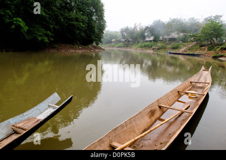 LUANG NAMTHA, Laos — Holzboote ruhen an den Ufern des Flusses Nam Tha in Luang Namtha, Nord-Laos. Diese traditionellen Schiffe dienen als lebenswichtige Transport- und Fischereigeräte für die lokalen Gemeinden und zeigen die dauerhafte Bedeutung des Flusslebens in dieser Region. Stockfoto