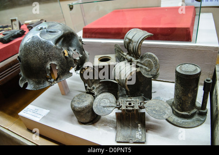 HANOI, Vietnam — Eine Vitrine im Vietnam Military History Museum zeigt verschiedene Arten von Granaten und kampfbeschädigten Helmen mit Schrapnell. Das 1956 gegründete Museum beherbergt umfangreiche Sammlungen militärischer Artefakte aus verschiedenen Konflikten. Diese Ausstellung dokumentiert die physischen Beweise von Kampfeinsätzen durch erhaltene Kampfmittel und Schlachtfeldartefakte. Stockfoto