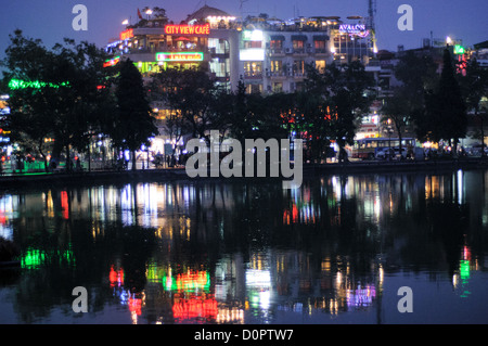 HANOI, Vietnam – die Lichter der Altstadt von Hanoi reflektieren nachts das stille Wasser des Hoan Kiem Lake (Ho Hoan Kiem). Die Mauer des Sees an diesem Ende ist von Scheinwerfern umgeben, die ihre Farbe ändern. Dahinter befinden sich die Lichter von Touristenbars und Restaurants mit Blick auf den See. Stockfoto