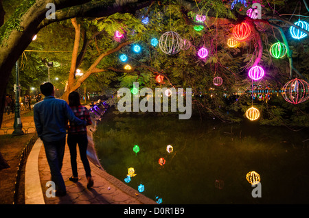 HANOI, Vietnam – farbenfrohe Lichter, die an Bäumen hängen, beleuchten den Küstenweg rund um den Hoan Kiem Lake im Zentrum von Hanoi. Ein paar Spaziergänge entlang der Uferpromenade unter dem beleuchteten Baldachin. Der historische See im Herzen der Altstadt von Hanoi ist ein beliebter Treffpunkt am Abend. Stockfoto