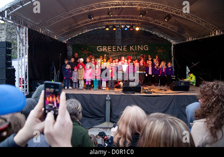 Grundschule Kinder singen auf der Bühne in der Öffentlichkeit, Bury St Edmunds Weihnachtsmarkt, Suffolk England Großbritannien Stockfoto