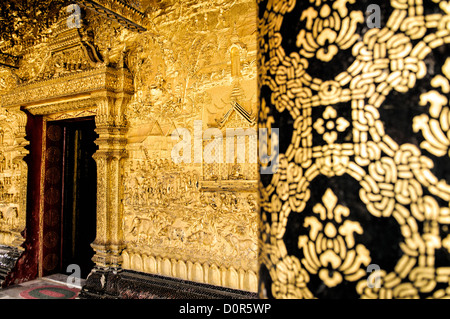 LUANG PRABANG, Laos - Schwarz und Gold Spalte auf der rechten Seite mit der komplizierten gold Außenwände bei Wat Mai Suwannaphumaham. Wat Mai, wie es oft genannt wird, ist ein buddhistischer Tempel in Luang Prabang, Laos, in der Nähe des Royal Palace Museum entfernt. Es wurde im 18. Jahrhundert erbaut und ist eines der am meisten reich verzierte Wats in Luang Prabang. Stockfoto