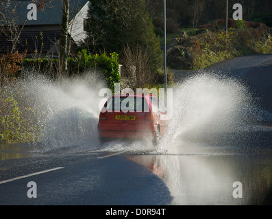 Rotes Auto getrieben durch stehendes Wasser auf der überfluteten Straße, Cumbria, England UK Stockfoto